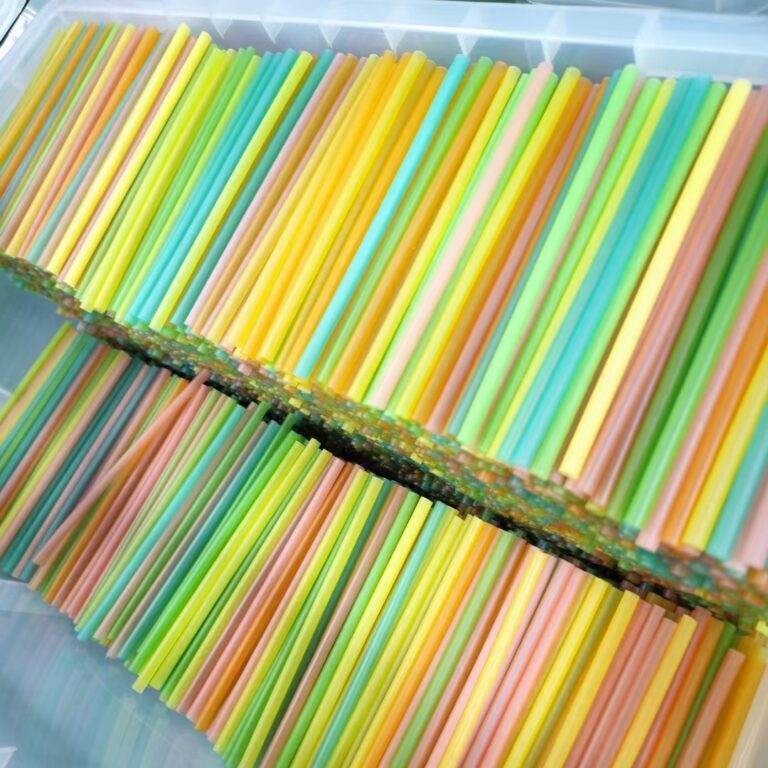 These drinking straws made of colored pasta, including green, yellow, pink, purple, blue and orange. The straws are placed next to each other on a white background and appear to be of varying lengths. They are cylindrical in shape with a hollow center, and their ends are cut at a slight angle to facilitate drinking.