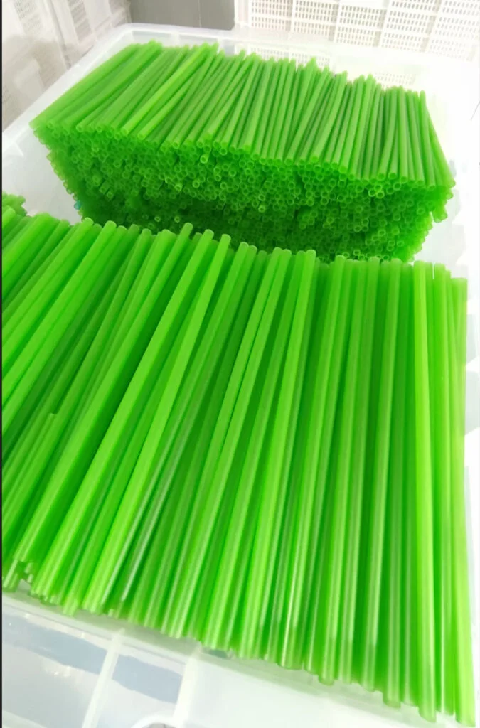 L'image des pailles de pâtes dans une boîte. Les pailles sont de forme cylindrique. Elles ont une couleur verte et une texture lisse. Elles sont disponibles pour les boissons chaudes et froides.