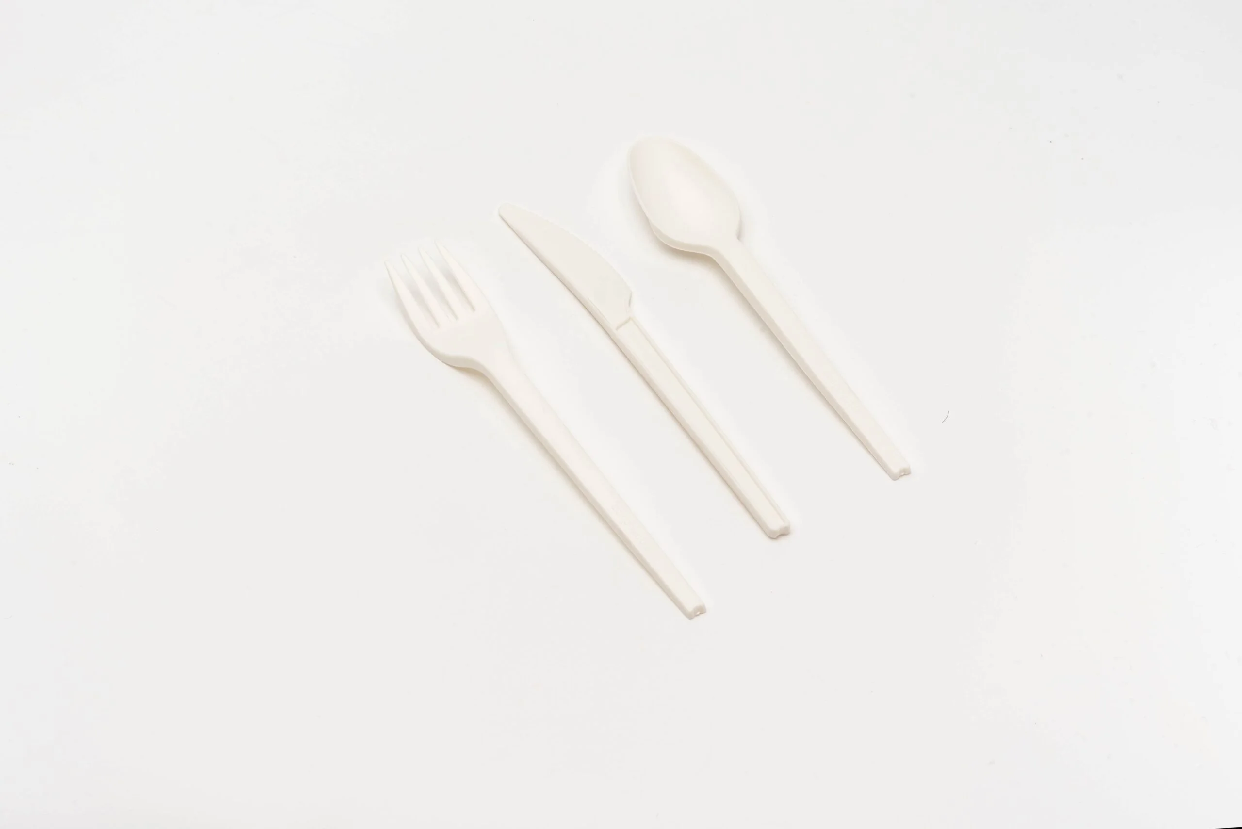 심플한 배경에 깔끔하게 배치된 PLA 커틀러리 세트입니다. 포크, 나이프, 스푼으로 구성된 이 세트는 재생 가능한 자원에서 추출한 생분해성 생체 활성 열가소성 플라스틱인 폴리락틱산(PLA)으로 제작되어 기존의 플라스틱 식기에 대한 지속 가능하고 친환경적인 대안을 구현합니다.
