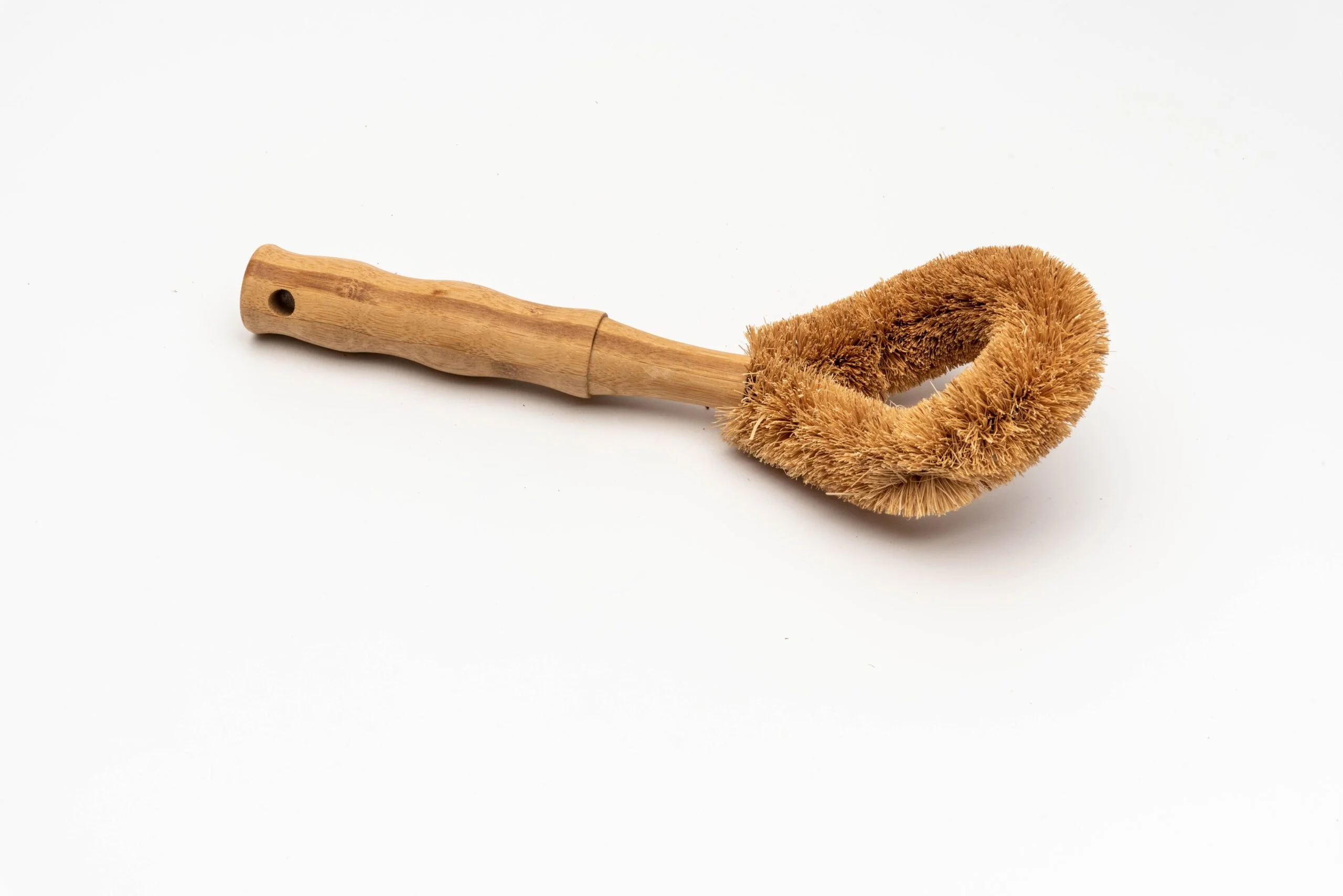 A imagem mostra uma escova de pratos com cerdas de fibra de coco e cabo de bambu.