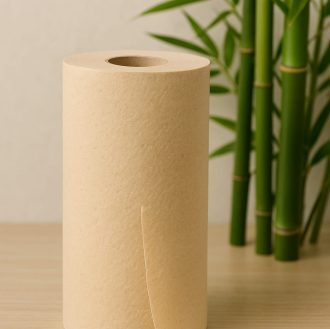 A roll of unbleached bamboo pulp kitchen paper standing upright on a wooden surface, with green bamboo stalks in the background, highlighting its natural and eco-friendly design.